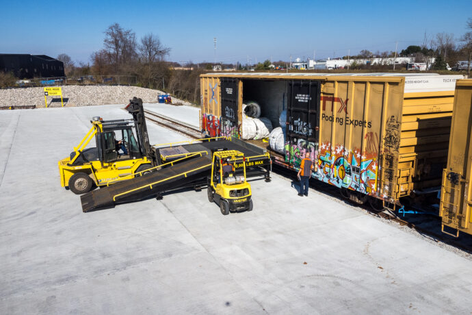 A King Steel worker uses a flat bed truck to unload steel wire from a box car.